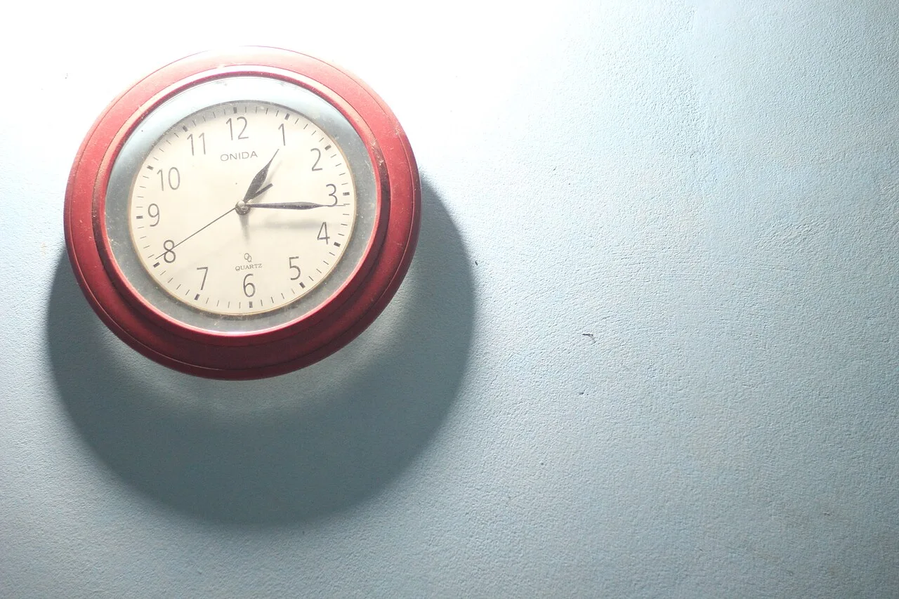 A red analogue clock on a pale wall