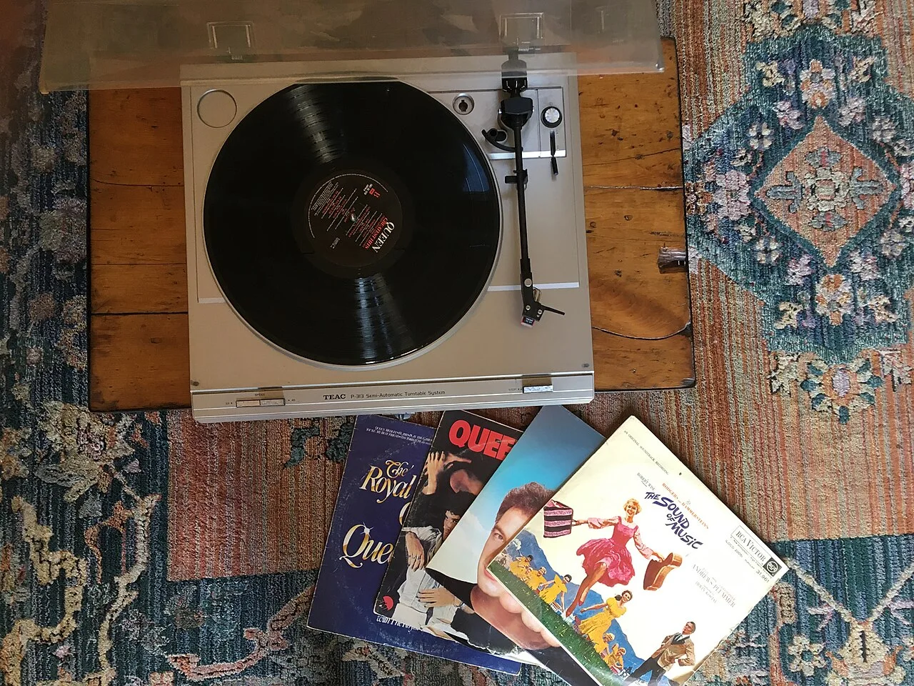 A vintage record player beside vinyl albums on a patterned rug